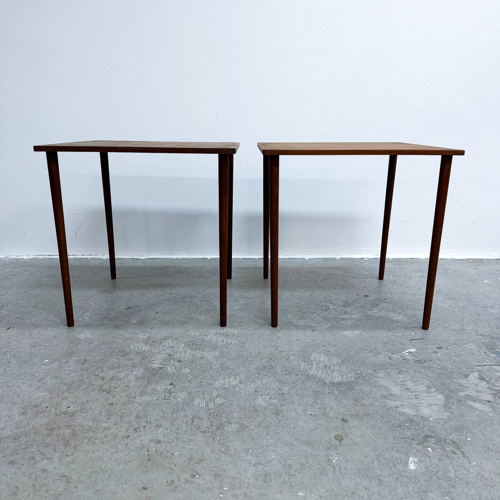 Two matching mid-century modern wooden tables with dark brown walnut-look tops and tapered legs, set against a plain white wall and concrete floor.