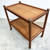 Wooden side table with two shelves on a concrete floor.