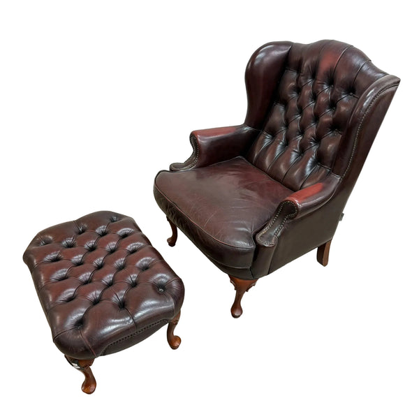 A dark brown leather wingback armchair with button tufting, shown with a matching leather ottoman on a light gray concrete floor against a white wall.