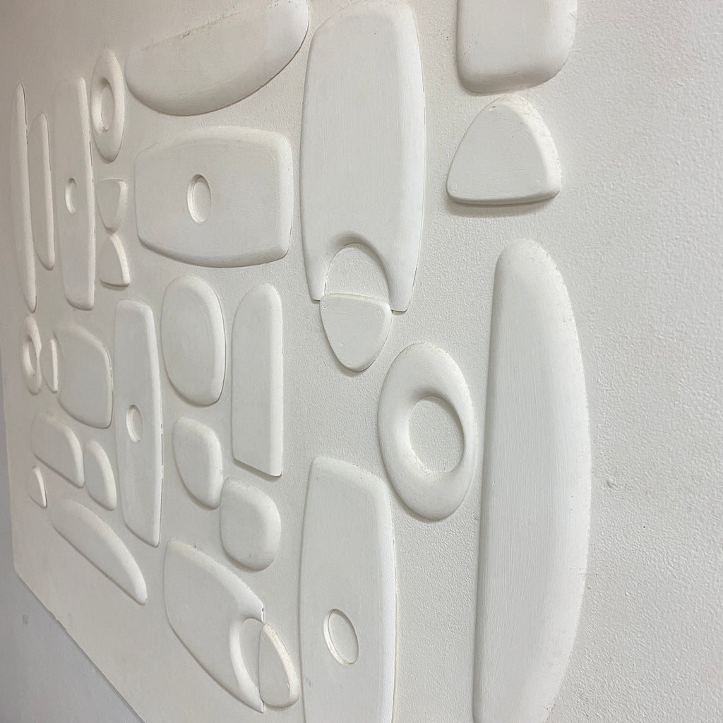 White textured wall art featuring a 3D abstract relief pattern of organic shapes and circles on a painted plaster-like surface.