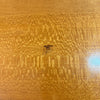 Close-up of a glossy wood surface with prominent swirling grain and a small dark insect near the center.