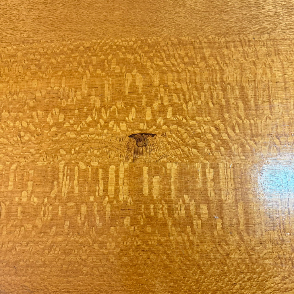 Close-up of a glossy wood surface with prominent swirling grain and a small dark insect near the center.