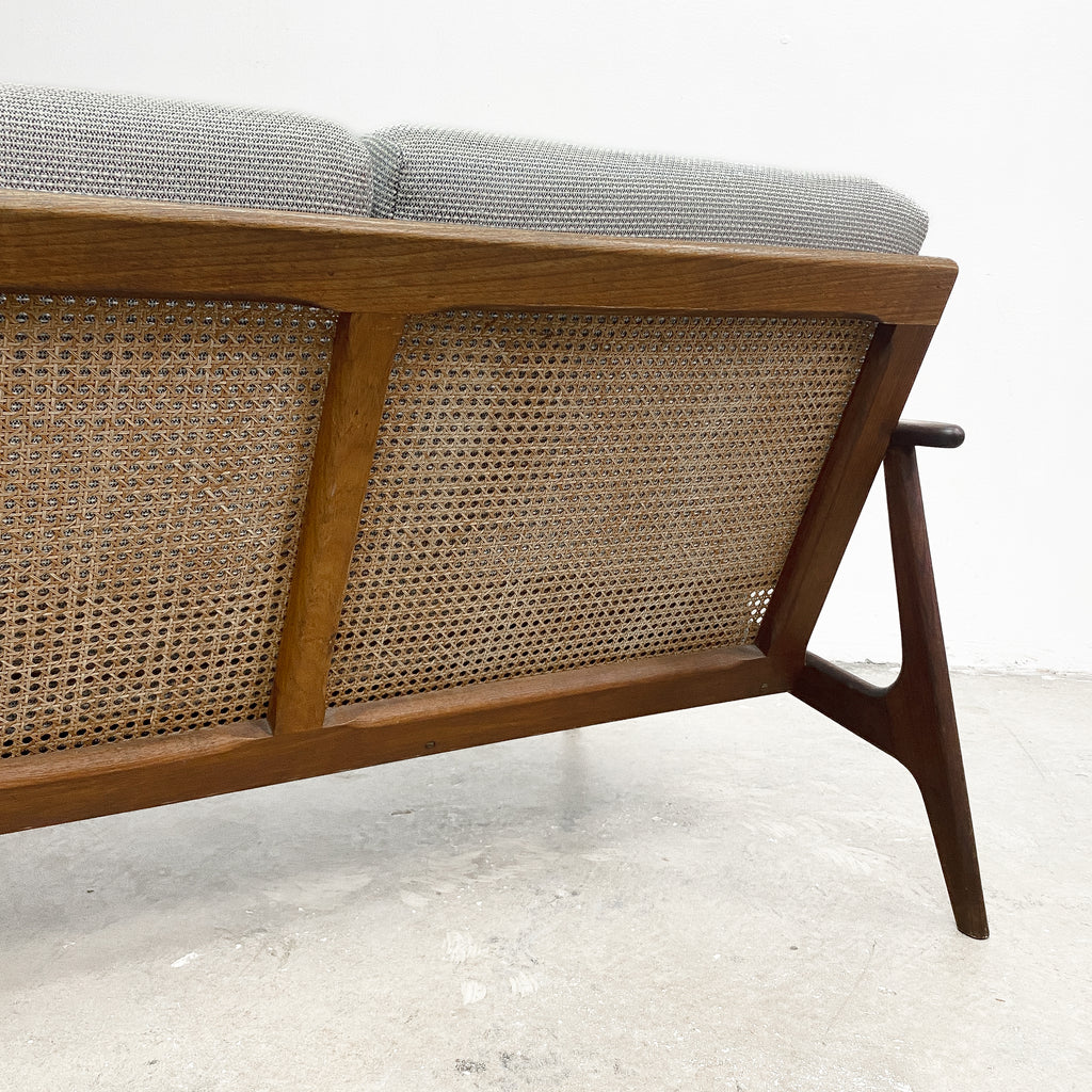 Wooden sofa with wicker backrest and gray cushions on a light background
