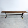 Wooden bench with black frame and yellow wheels on a gray floor against a white wall
