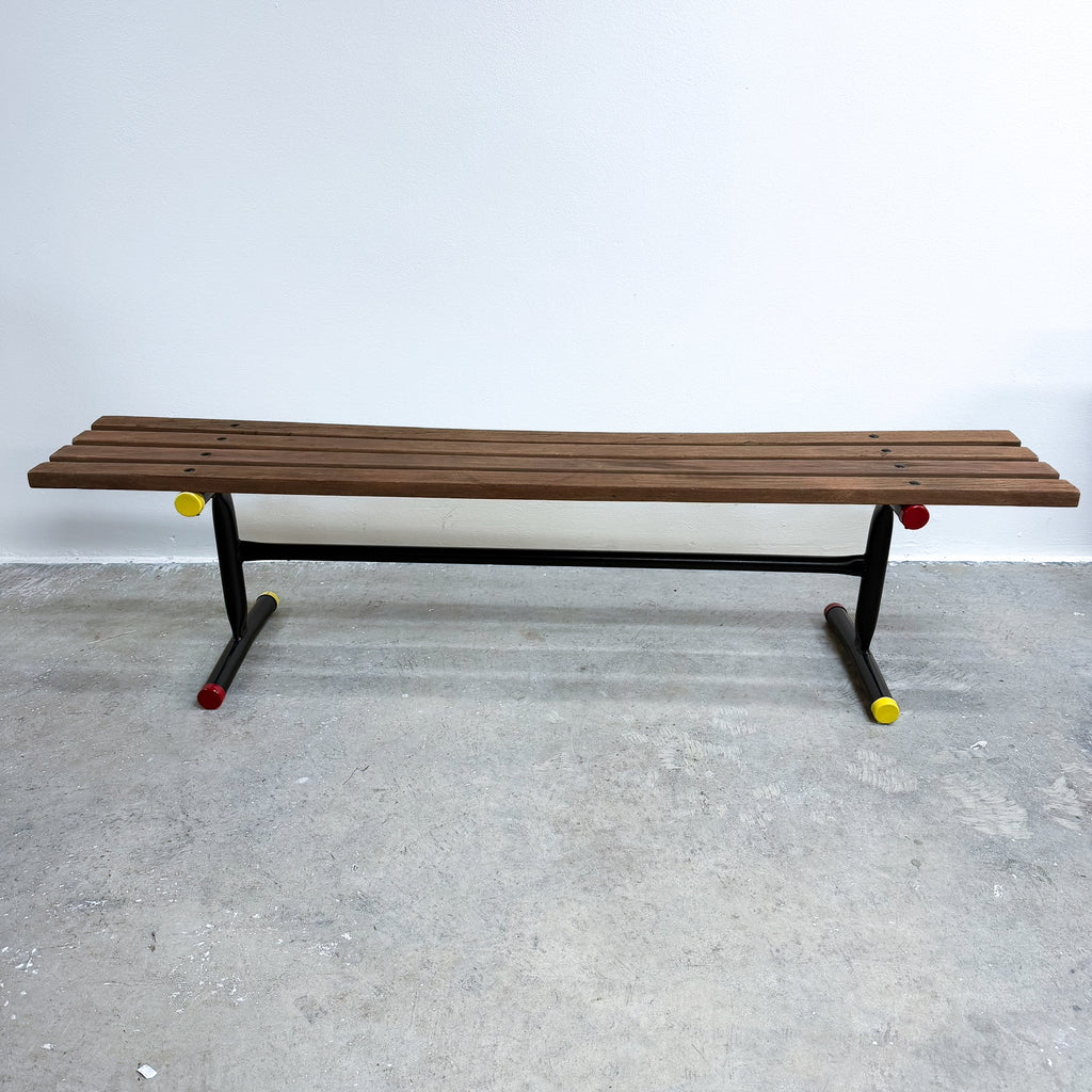 Wooden bench with black frame and yellow wheels on a gray floor against a white wall