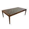 A mid-century modern rectangular coffee table with a dark mosaic tile top and a warm brown wood frame, photographed in a minimalist studio setting.