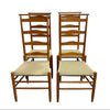 Four wooden dining chairs with woven beige and white checkered seats, arranged in two pairs against a plain white wall and concrete floor.