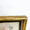 Gold-framed artwork with visible damage on a white wall