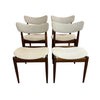 Four mid-century modern dining chairs with curved cream fabric seats and backs on dark wood frames, arranged in two pairs against a plain white wall and concrete floor.