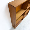 A mid-century modern wooden bookcase with a warm medium-brown finish, positioned against a white wall on a light gray concrete floor.