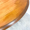 Close-up of a wooden round table with a light wood finish on a concrete floor.