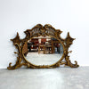 Decorative gold mirror with intricate designs on a white wall.