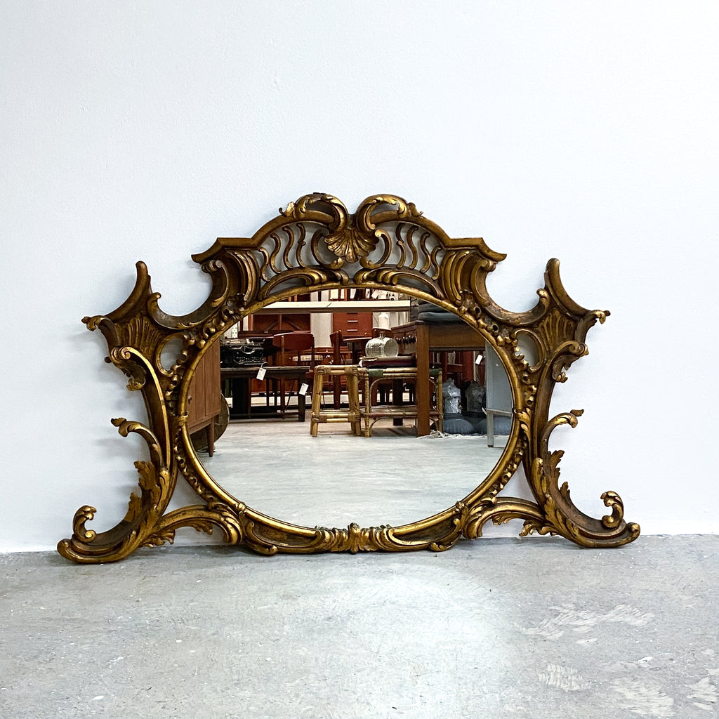 Decorative gold mirror with intricate designs on a white wall.