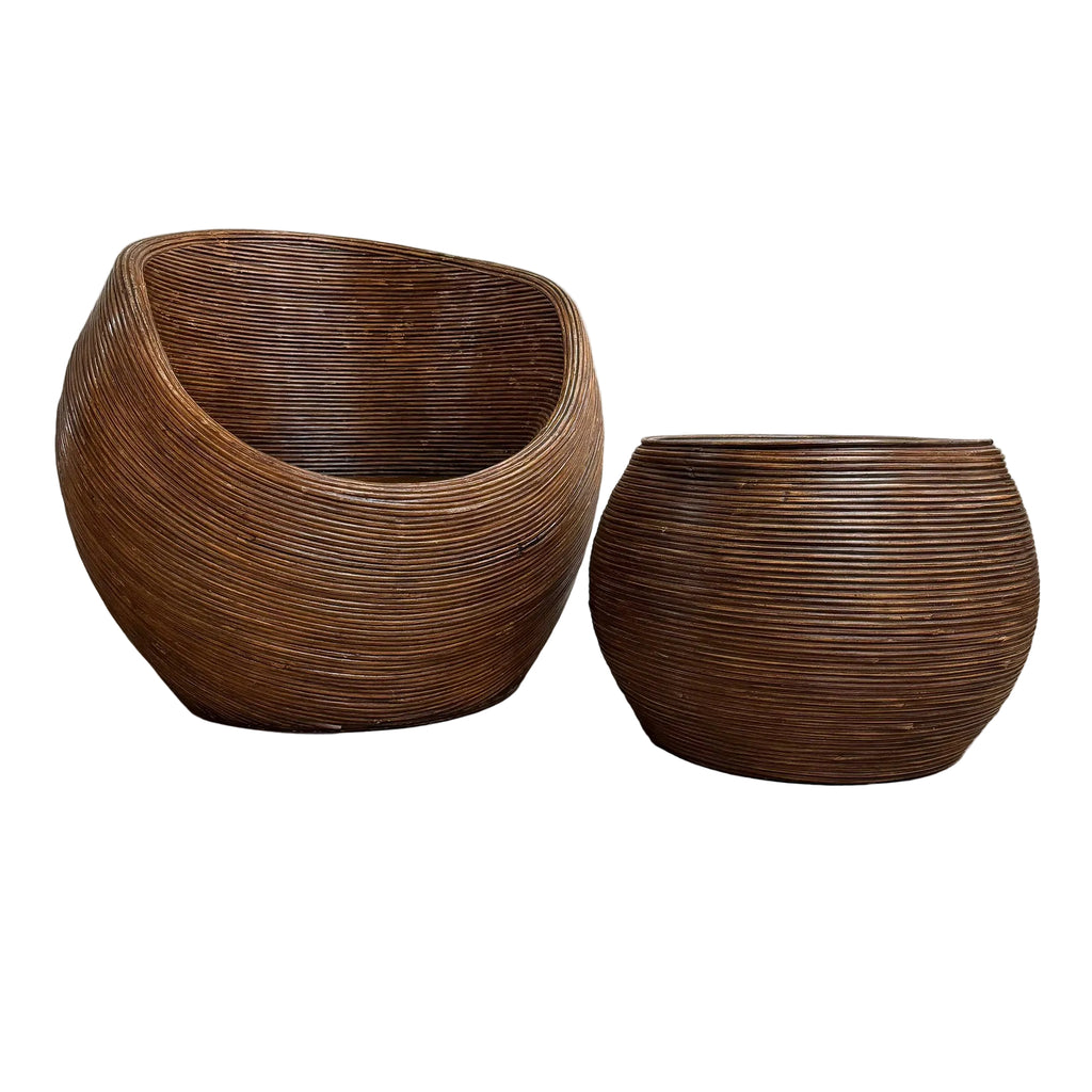 Two dark brown woven rattan furniture pieces, one a rounded shell-shaped chair and the other a matching round planter or pot, set on a concrete floor against a white wall.