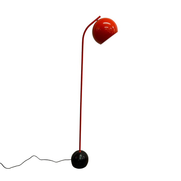 A modern floor lamp with a glossy Orange curved stem, a red spherical shade, and a black spherical base, standing on a concrete floor against a white wall.