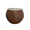 A round, ribbed brown side table with a glass top, set against a plain white wall and gray concrete floor.