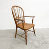 A classic wooden spindle-back armchair with turned legs and armrests, shown on a concrete floor against a white wall.