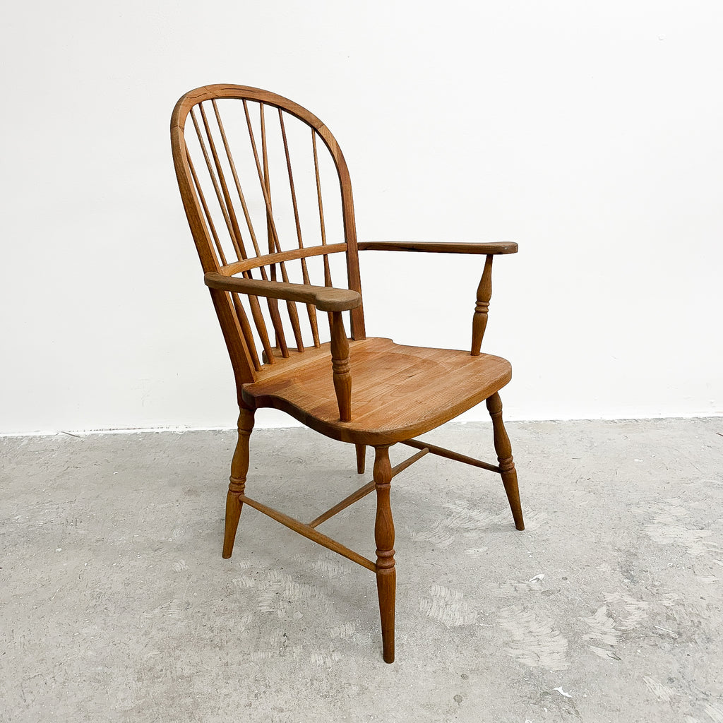 A classic wooden spindle-back armchair with turned legs and armrests, shown on a concrete floor against a white wall.