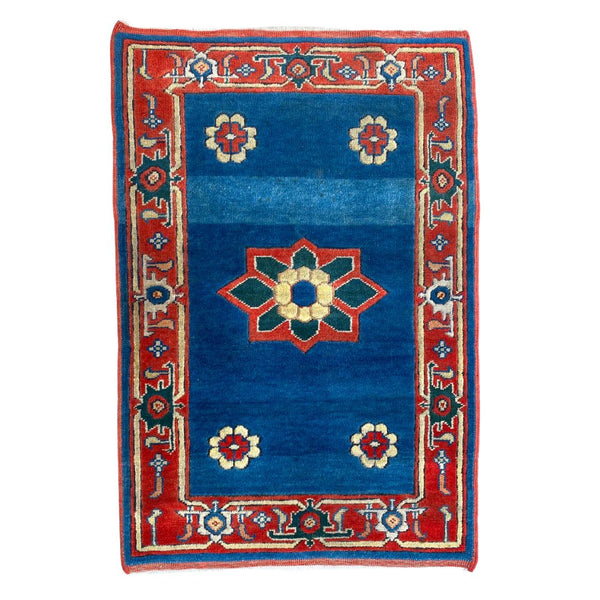 Decorative rug with blue center and red border featuring floral patterns on a white background