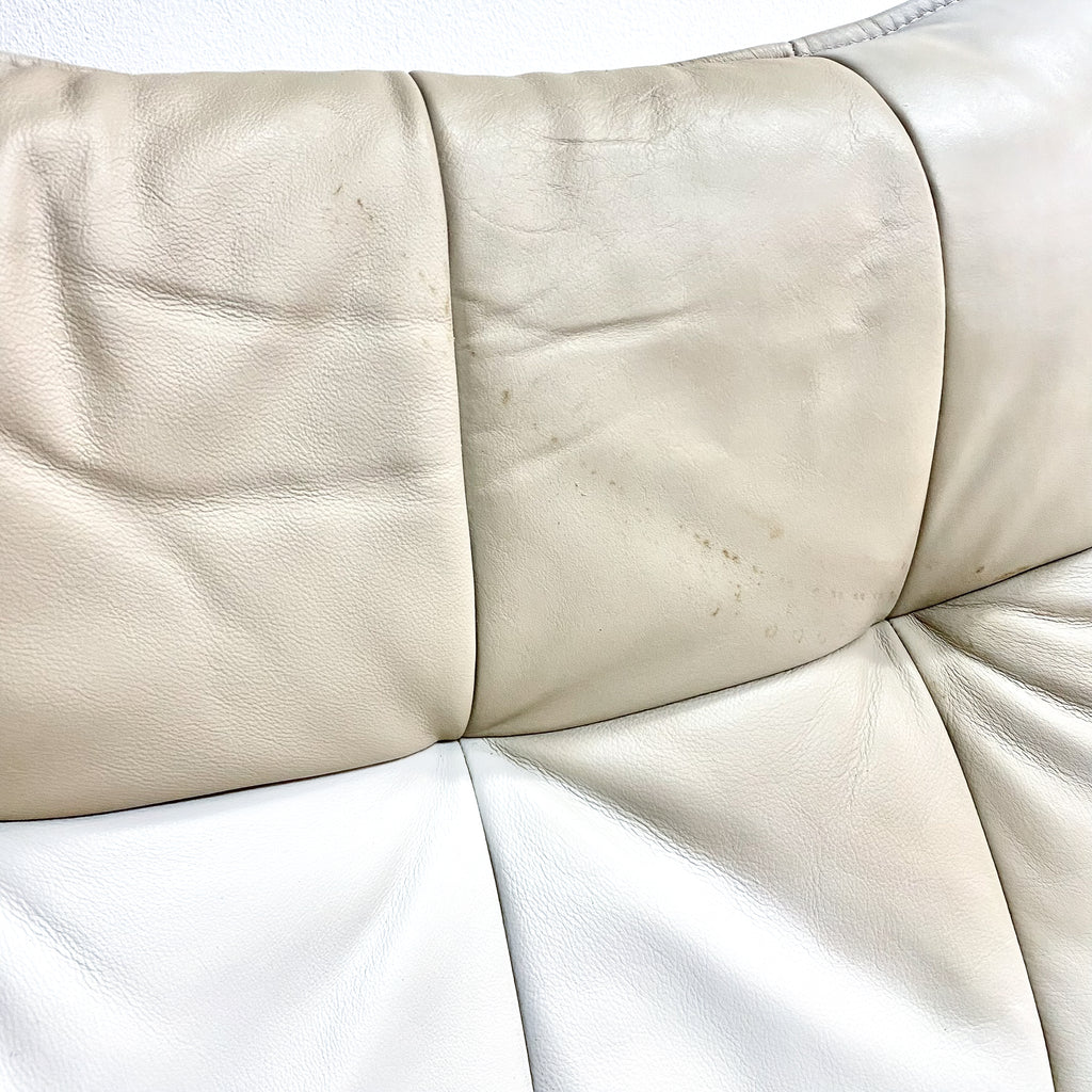 Close-up of beige leather sofa with visible wear and tear on a white background